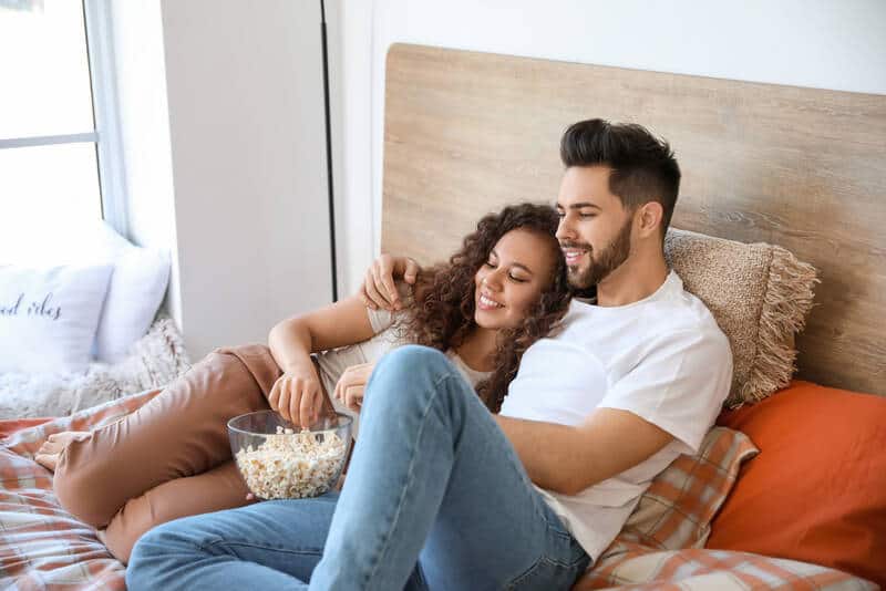Happy young couple having a movie while lying on bed eating popcorn.