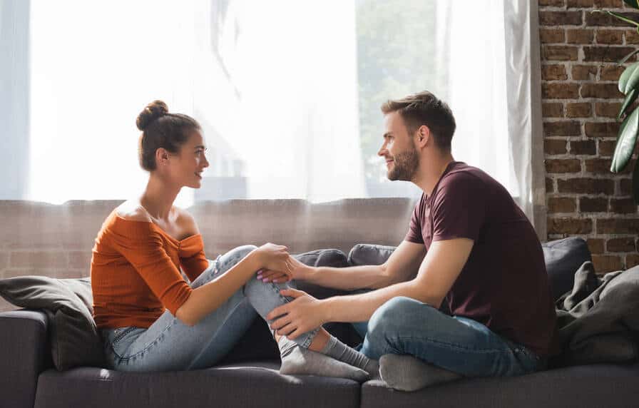 Couple sitting on sofa facing each other smiling and talking.