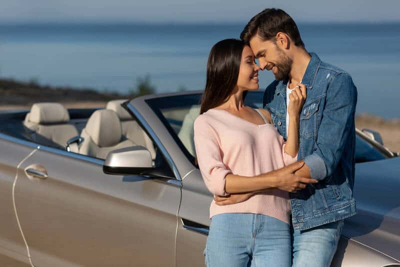 Woman and man smiling touching noses while leaning against car
